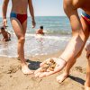 Persone sulla spiaggia, una mano con conchiglie in primo piano.