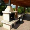 Un barbecue in pietra sotto un tetto di legno, con uno spazio esterno lastricato.