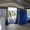 Interno di tenda con pavimento in legno, mobili bianchi e sedie all'esterno.