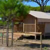 Tenda safari con veranda in legno, circondata da alberi.