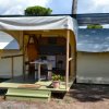 Una tenda con veranda arredata con tavolo e sedie, situata in un'area ombreggiata da alberi.