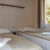 Due letti singoli con lenzuola, finestra con tende a righe e una mensola a muro.