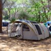 Una tenda familiare in un campeggio boschivo con ombre e altre tende intorno.