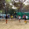Persone che giocano a pallavolo in un campo sabbioso, circondato da alberi.