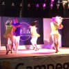 Persone su un palco ballano con illuminazione colorata.