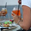 Due persone tengono cocktail arancioni e bianchi su un tavolino con stuzzichini.