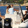 Persone a bordo di un gommone con due motori in un mare calmo, costa rocciosa in lontananza.