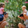 Bambini sorridenti sulle spalle di due adulti in un giardino fiorito.