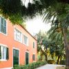 Edificio arancione con persiane verdi e palme circostanti.