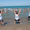 Tre istruttori sulla spiaggia guidano un gruppo di persone in acqua.