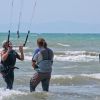 Persone fanno kitesurf in mare, con attrezzatura e caschi protettivi.