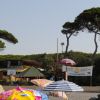 Spiaggia con ombrelloni colorati, pini mediterranei, e strutture di legno.