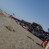 Una spiaggia con ombrelloni blu e viola, persone in acqua e cartello giallo sulla sabbia.