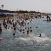 Spiaggia affollata con persone che nuotano nel mare e ombrelloni colorati sulla sabbia.