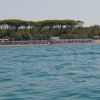 Mare azzurro con spiaggia affollata di ombrelloni e alberi sullo sfondo.