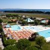 Vista piscina con ombrelloni arancioni, giardino verde e mare sullo sfondo.