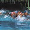 Bambini in gara in piscina con cuffie e palette, schizzano mentre nuotano.